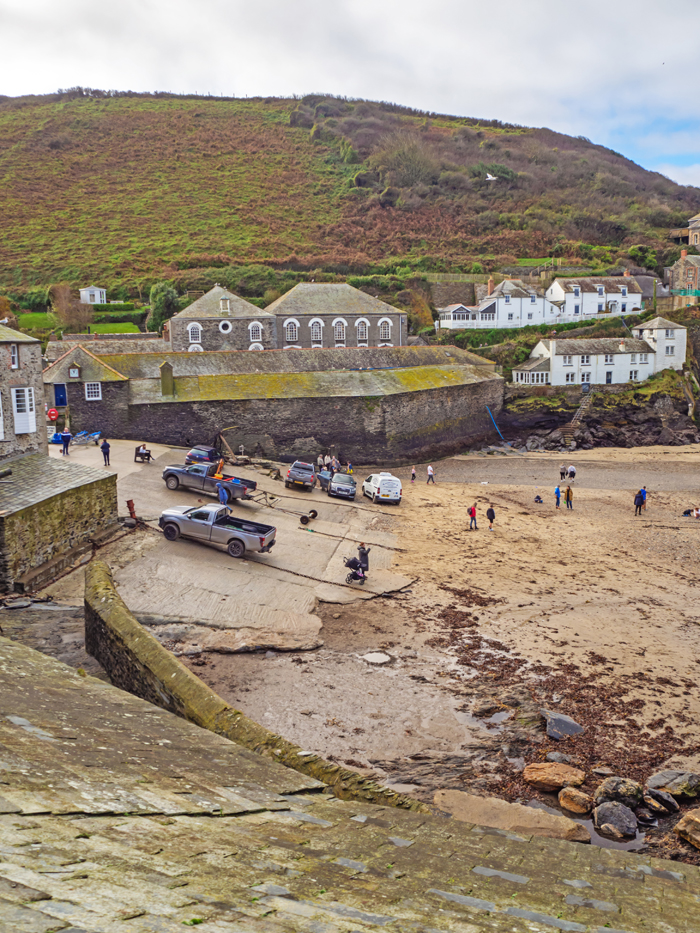 Boats and pickup trucks on a harbour slipway with houses and cliffs
